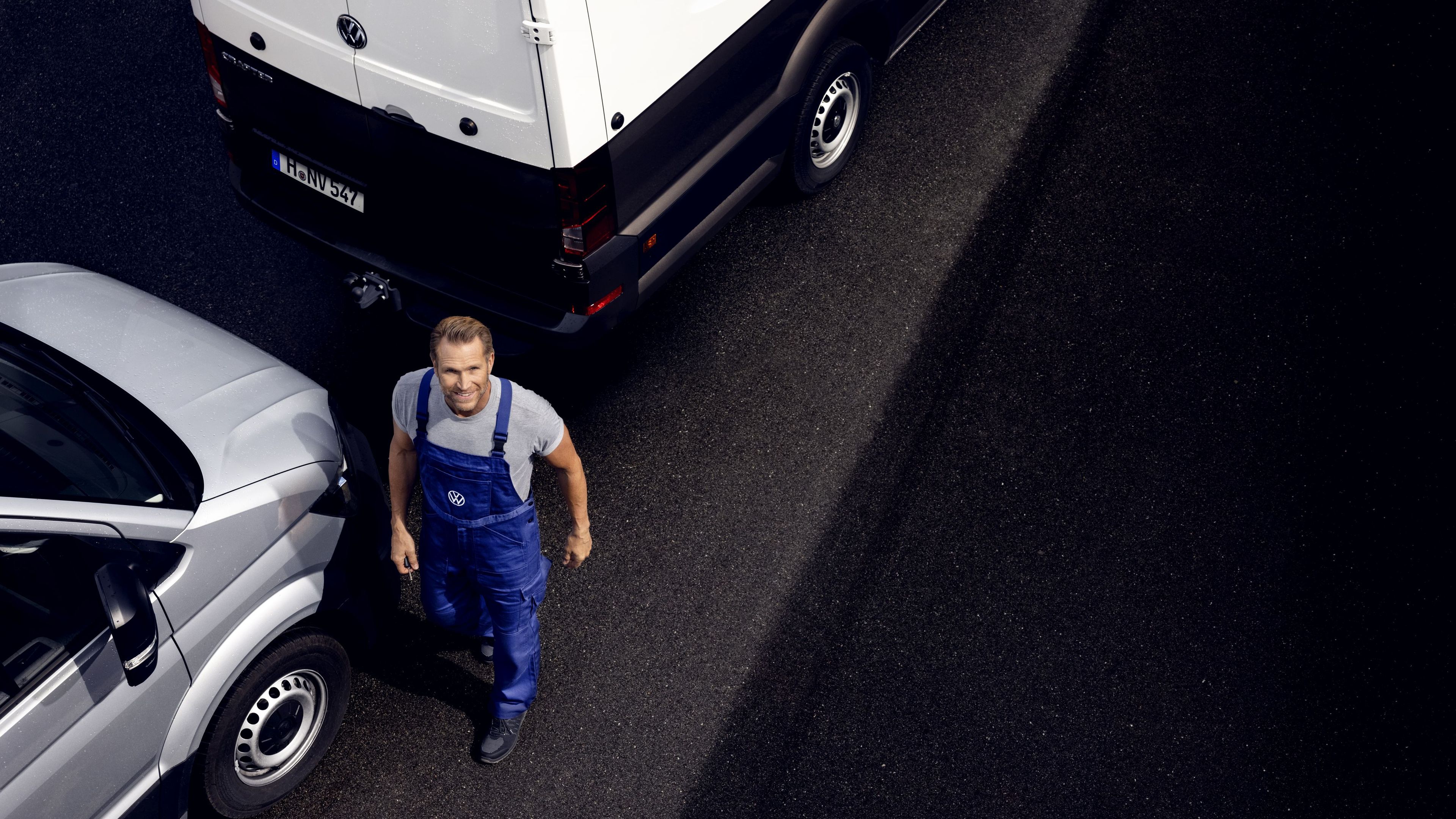 Сервизен техник на Volkswagen между товарни автомобили Мъж в работен гащеризон Volkswagen стои между два сиви товарни автомобила